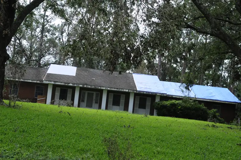 A blue tarp covering storm damage on the roof of a brick ranch house.