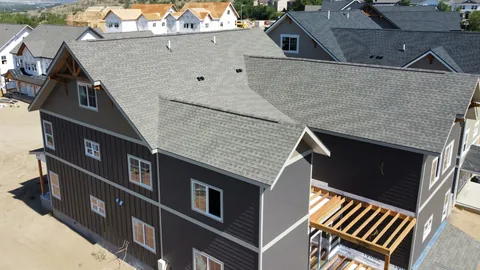 Gray architectural shingles finished on a new townhome with dark siding, framed units behind it, seen from above.