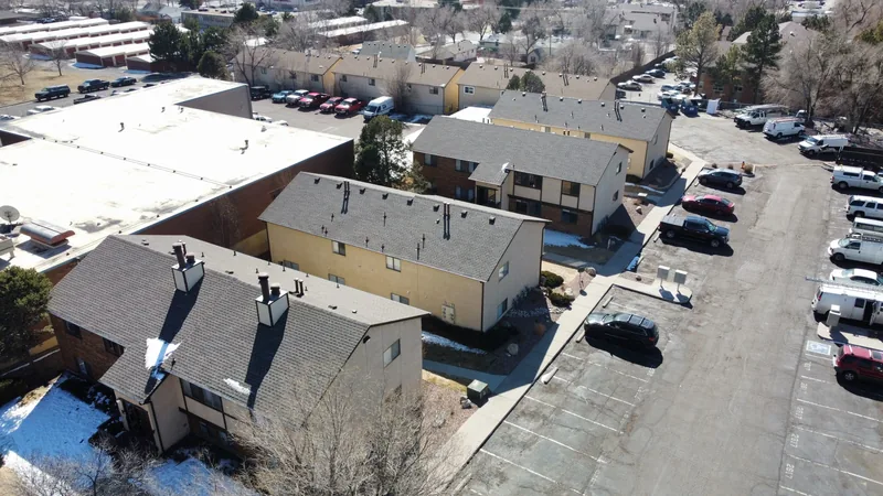 Apartment complex seen from above, with gray shingle gables, white flat roofs and a full parking lot.