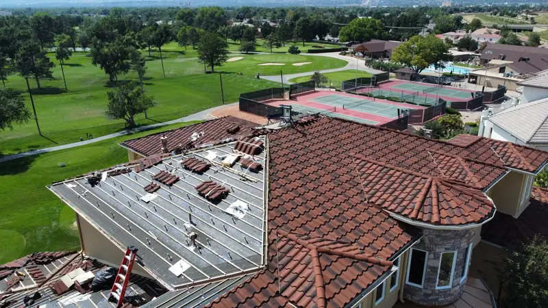 Red clay tile roof partly torn off on a house with a stone turret, beside a golf course.