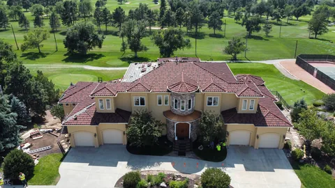 Front view of a large stucco house with a nearly finished red clay tile roof, beside a golf course.