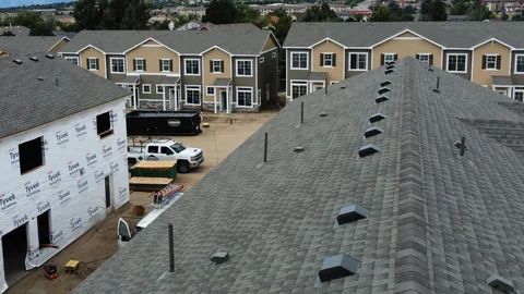 Finished gray shingle roof in the foreground, with house-wrapped townhomes and tan finished townhomes behind it.