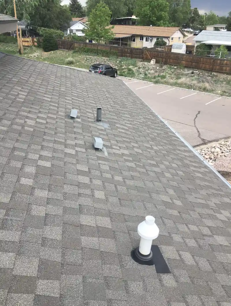 Close-up of a finished gray architectural shingle slope with a white plumbing vent and small roof vents.