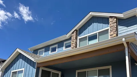 Blue lap and board-and-batten siding with stone columns, white gutters and a wide covered patio.