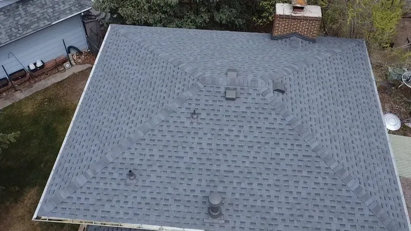 Overhead view of a gray shingle hip roof with ridge caps, roof vents and a brick chimney.