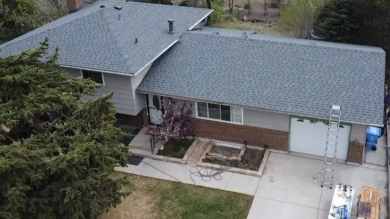 Overhead view of a gray shingle roof on a split-level brick house with a ladder at the garage.