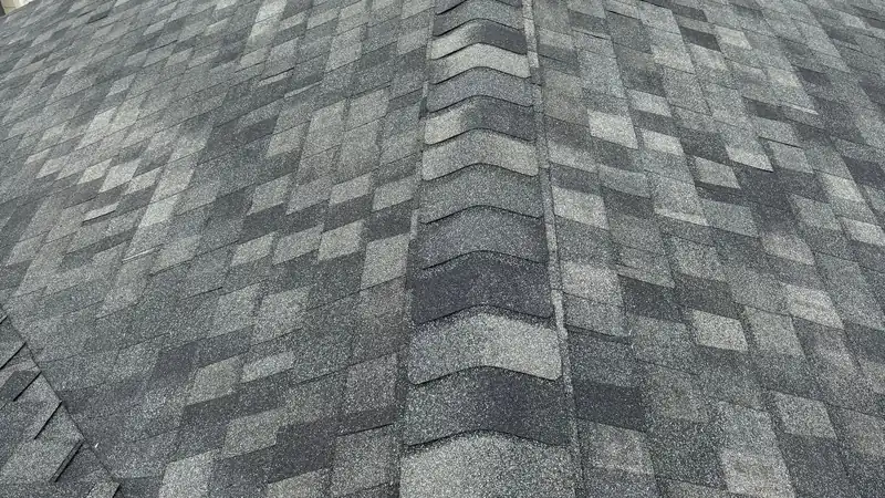 Close view of gray and charcoal architectural shingles meeting at a raised ridge cap.