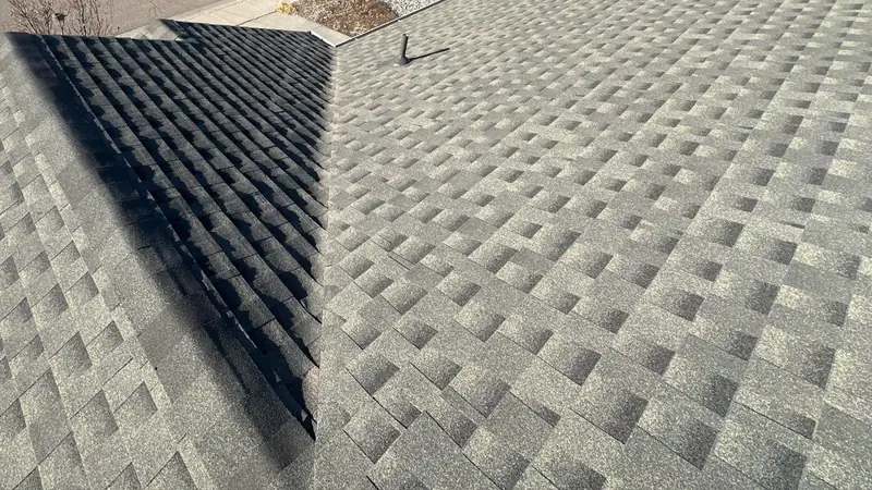 Roof valley where a shaded dark slope meets a sunlit plane of tan architectural shingles.