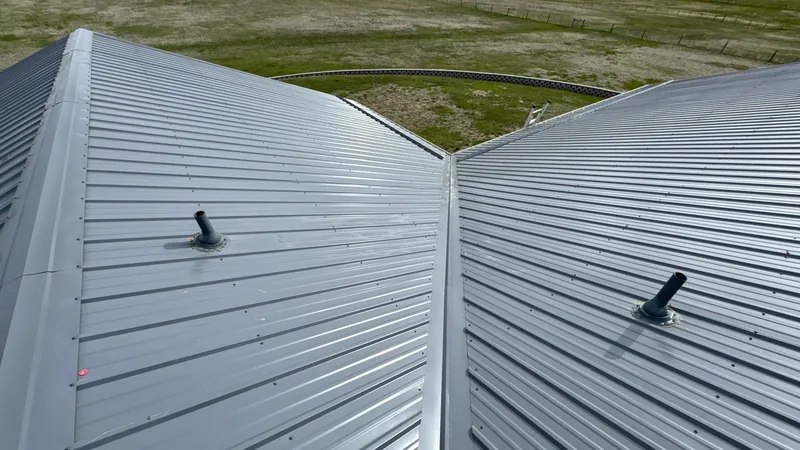 Gray ribbed metal roof valley with two black pipe boots above a green grassy field.