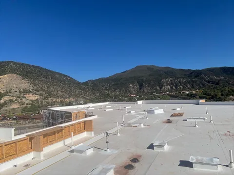 Wide white membrane roof with vents and curbs on a large building under a clear blue sky.