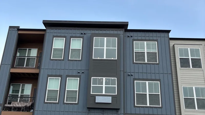Upper facade of a three-story building with dark blue vertical siding and white-framed windows.