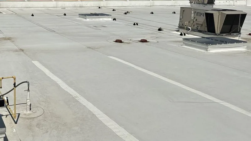Light gray membrane flat roof with walkway stripes, roof drains, skylights and a rooftop unit.