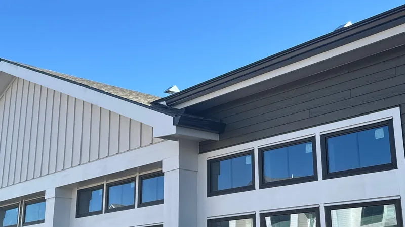 Gray lap siding, a white board-and-batten gable and black-framed windows below a shingle roof edge.