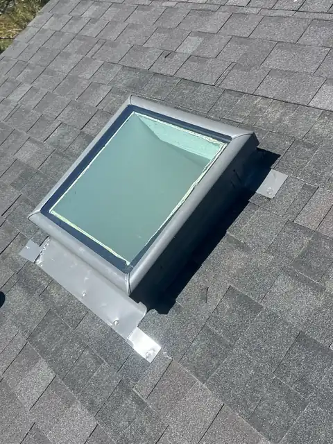 Skylight with metal step flashing set into dark gray architectural shingles.